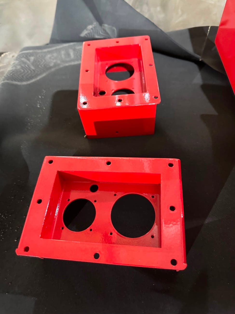 Two red coated metal housings with circular openings and mounting flanges