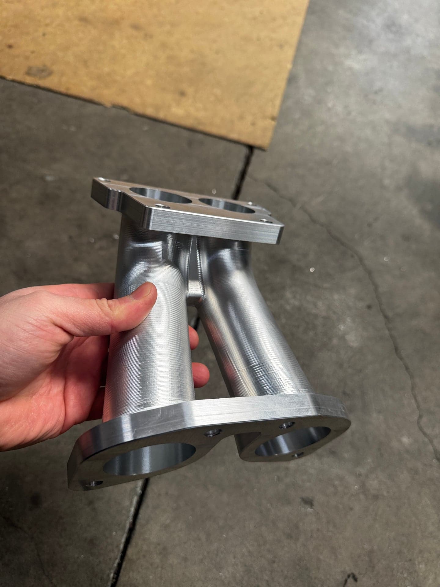 Angled view of a machined part with two hollow cylinders, end flanges and mounting holes
