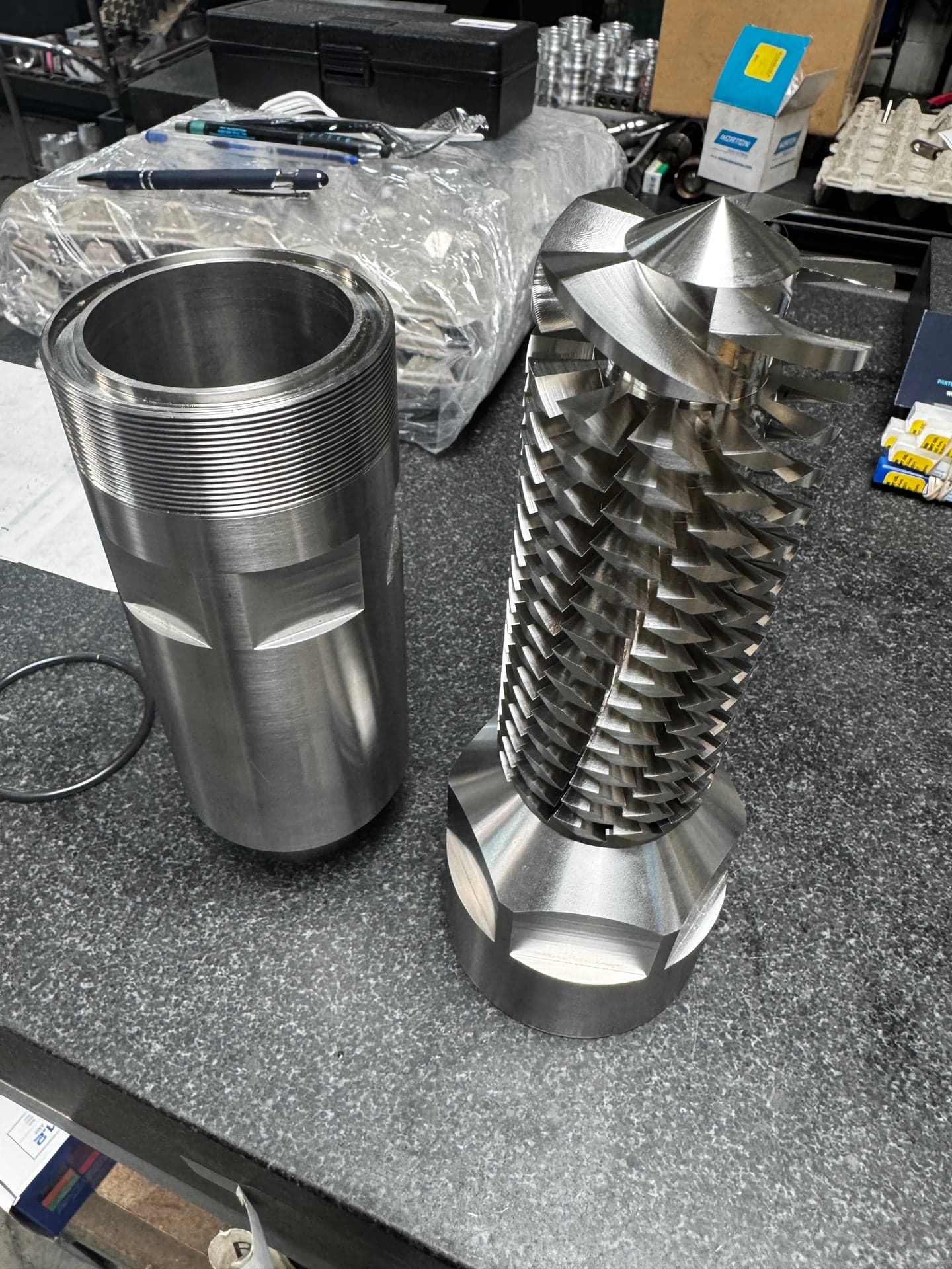 Hollow cylinder with external threads beside a cylindrical machined part with repeated angled grooves