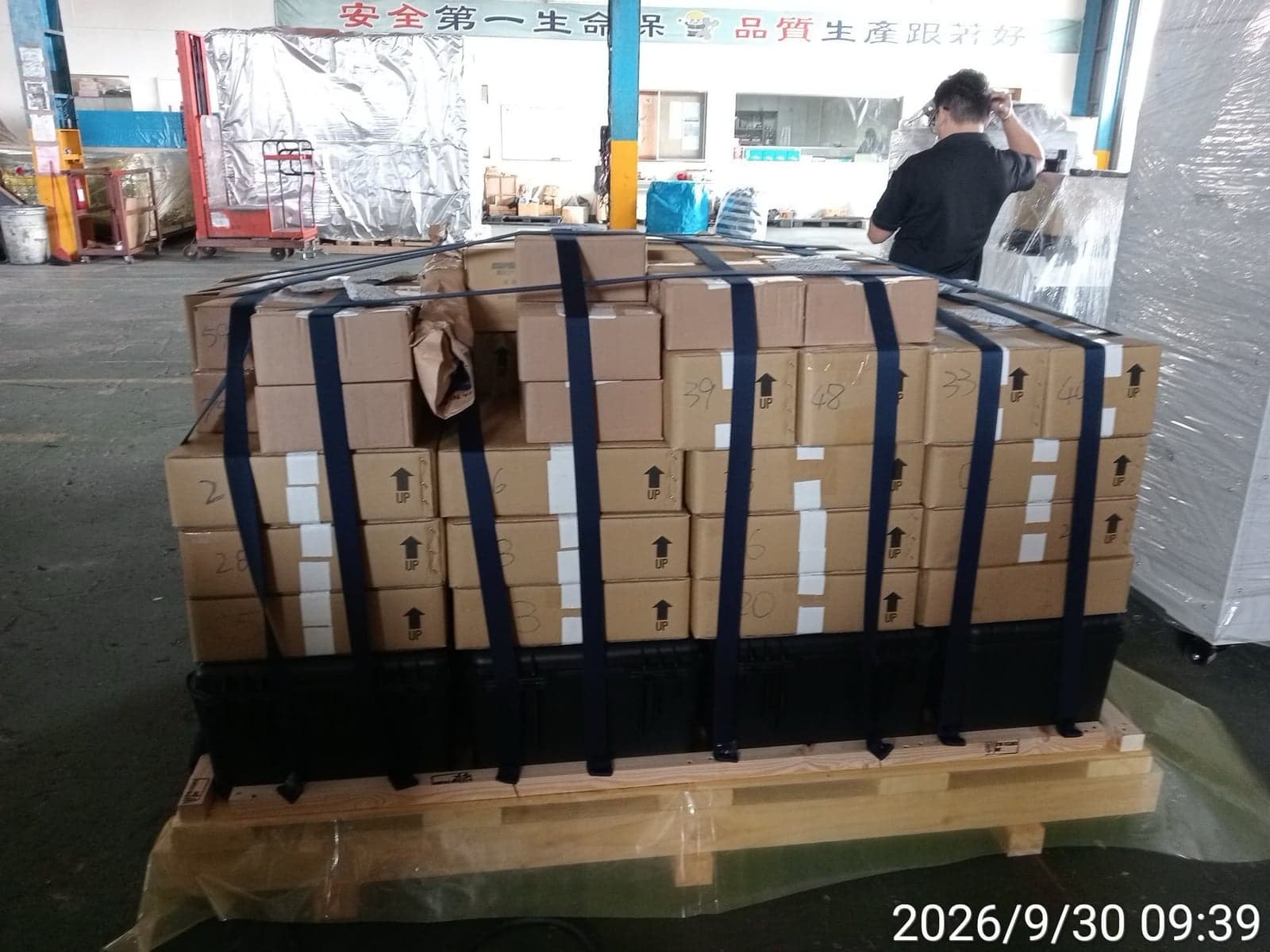Cartons and black protective cases secured with straps on a wooden pallet
